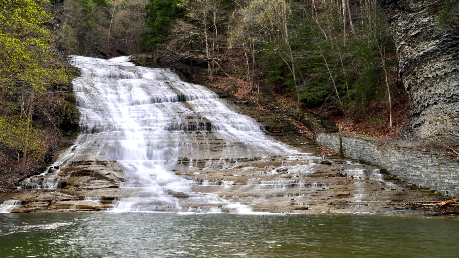 Buttermilk Falls cascading over broad rock ledges beside the stone gorge stairway in Ithaca, New York
