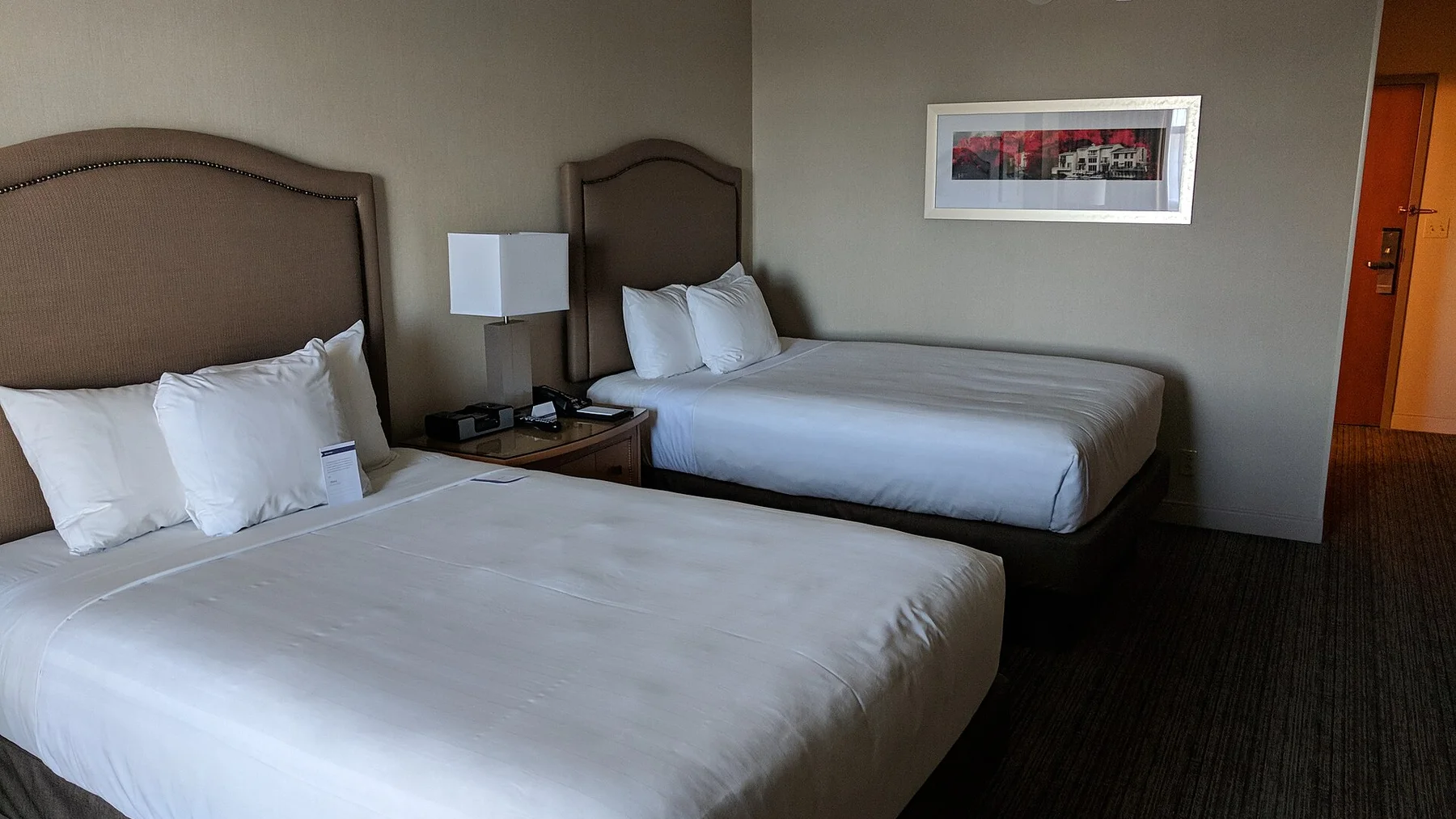A standard hotel room with two made beds, a shared nightstand and a clear path to the door