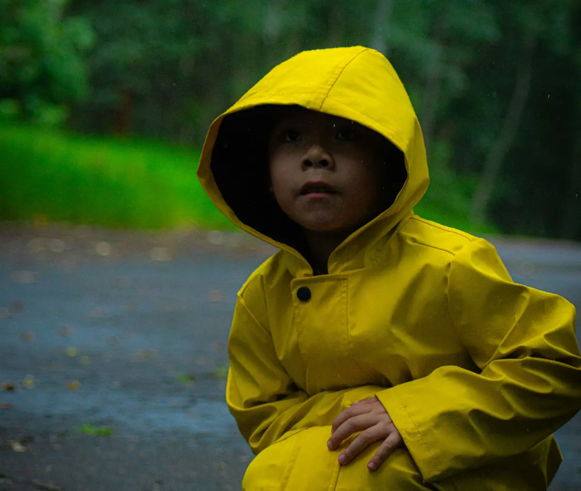 A child in a yellow rain jacket outdoors on a wet day