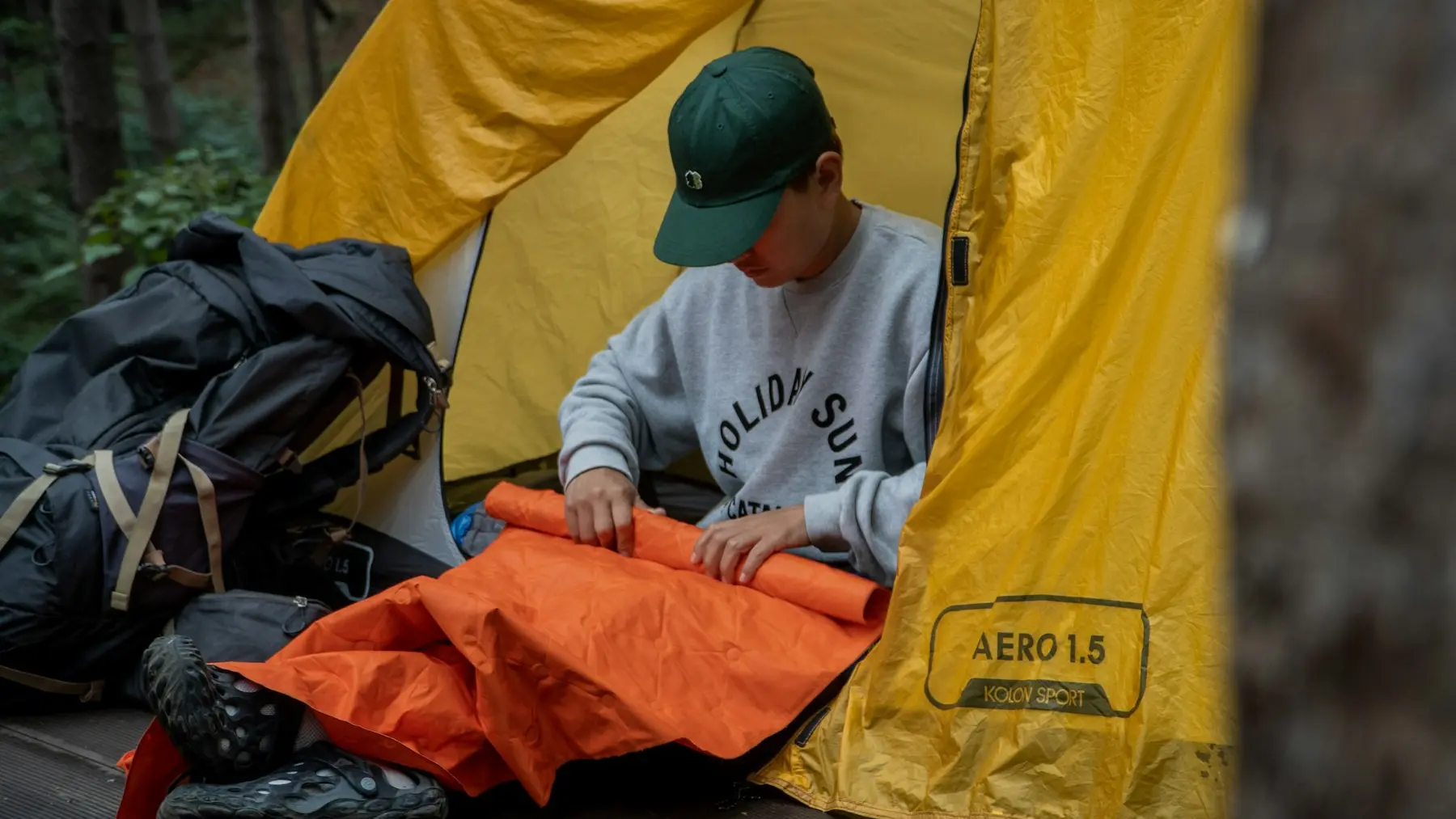 A camper arranging an orange sleeping pad inside a yellow tent