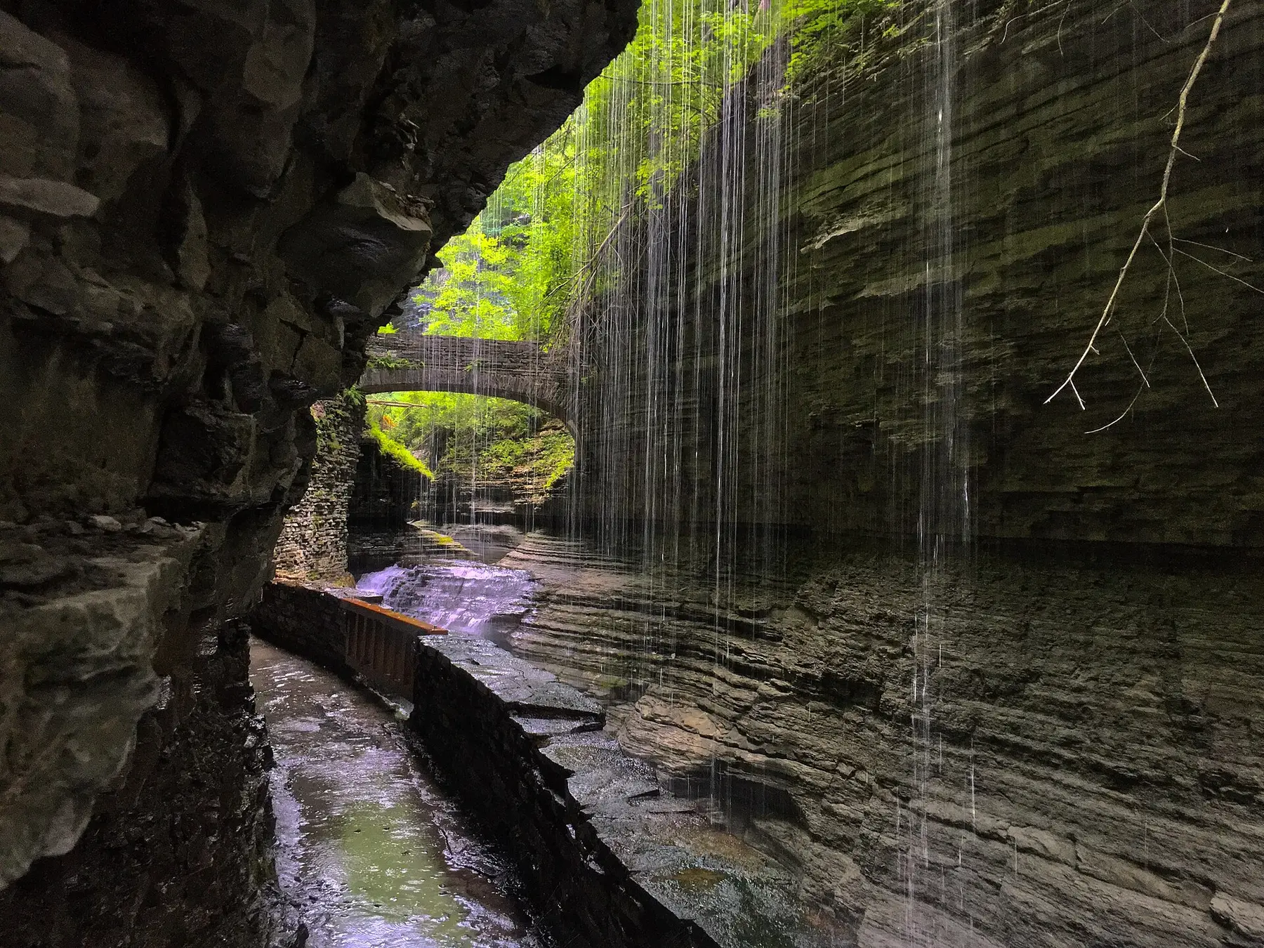 The Watkins Glen Gorge Trail passing behind a curtain of falling water beneath a stone bridge